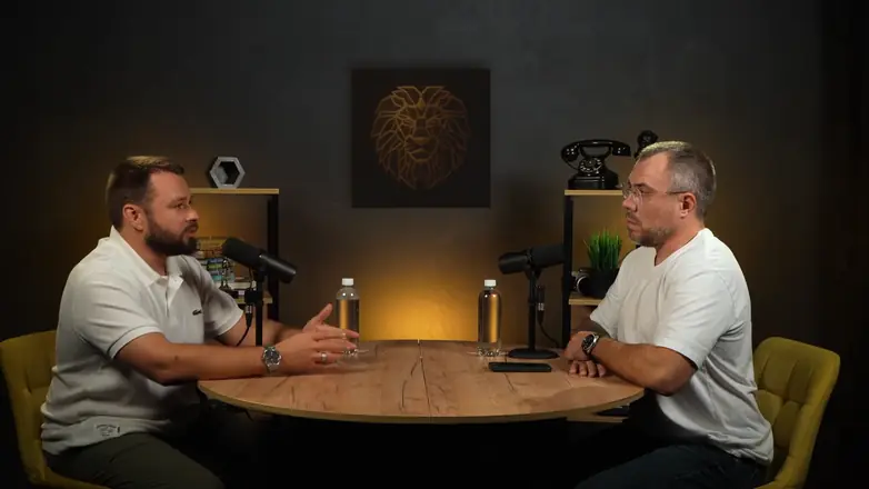 A two-person business podcast at a round table with two microphones, filmed with several cameras