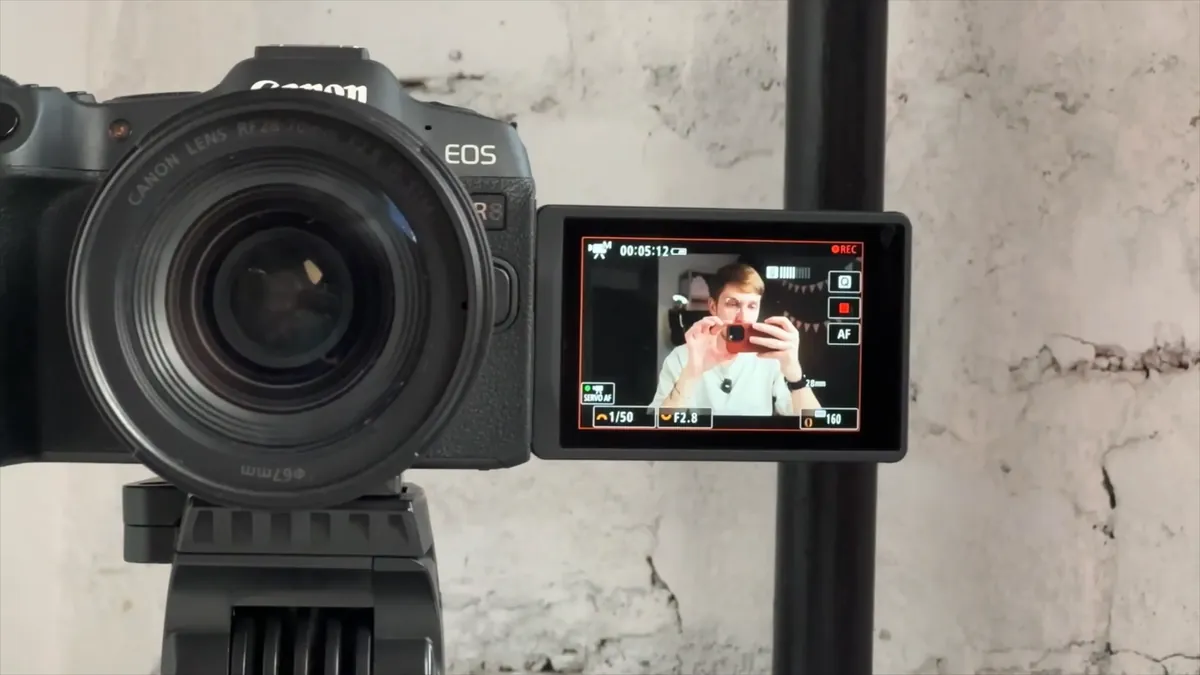 A Canon mirrorless camera on a tripod with its flip screen showing Evgeny adjusting his setup