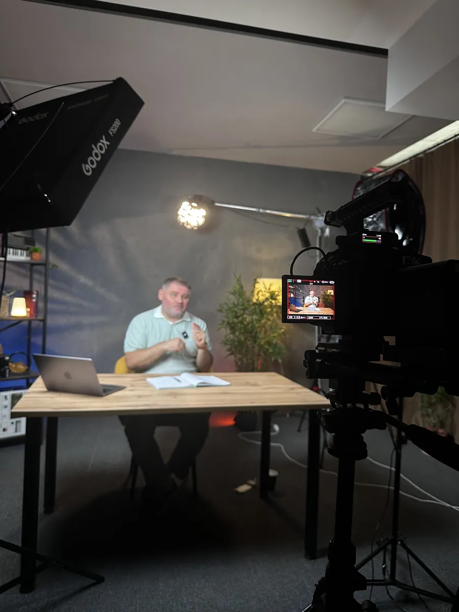 A studio shoot: a client at a wooden desk under softbox lights, with a camera and monitor in the foreground
