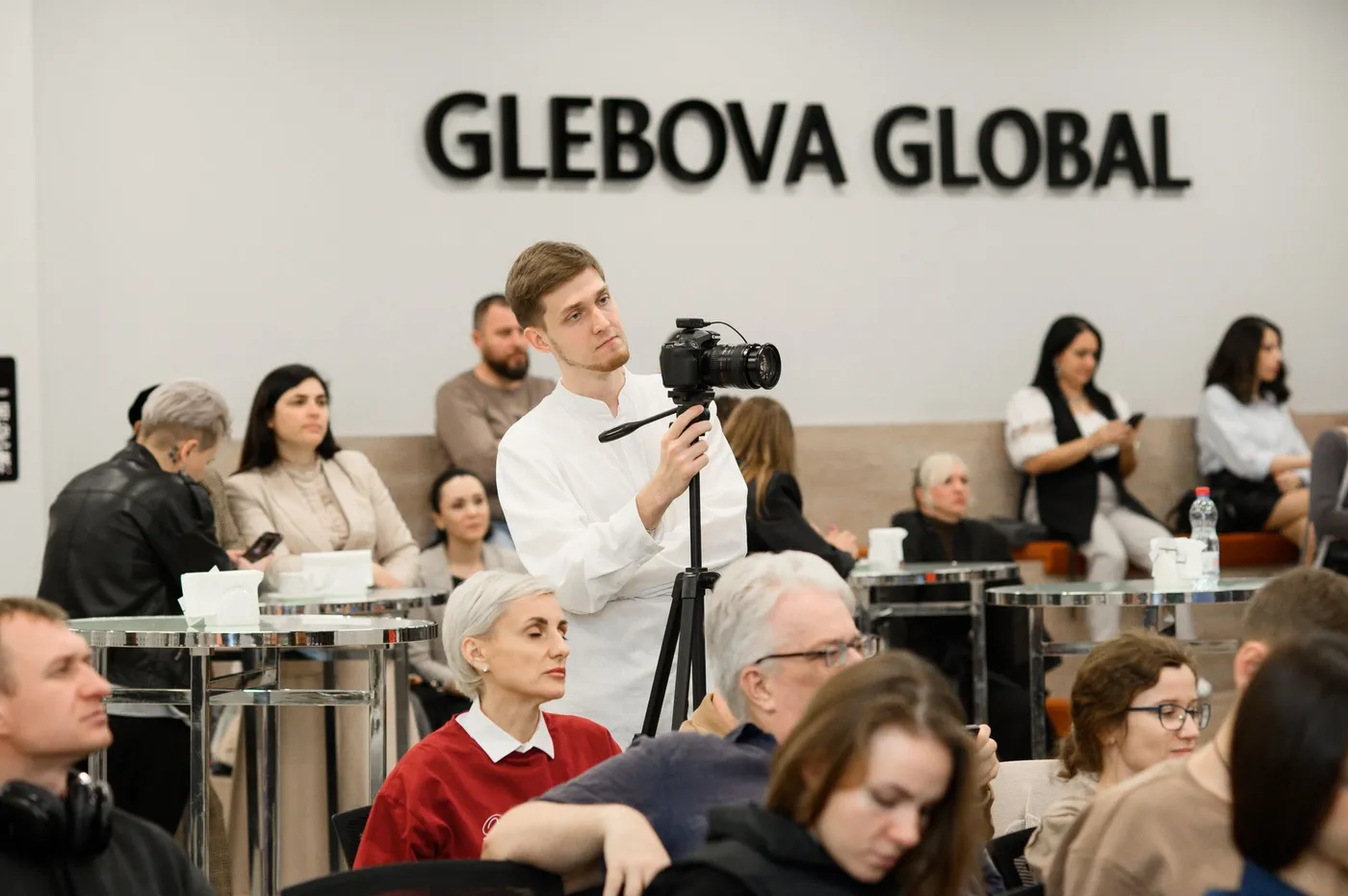 Evgeny Maximov filming a business event with a camera on a tripod, the audience around him