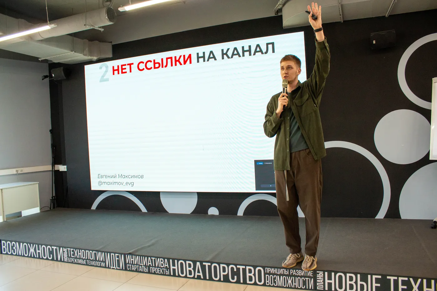 Evgeny Maximov on a stage with a microphone, raising his hand next to a large slide about a social media mistake