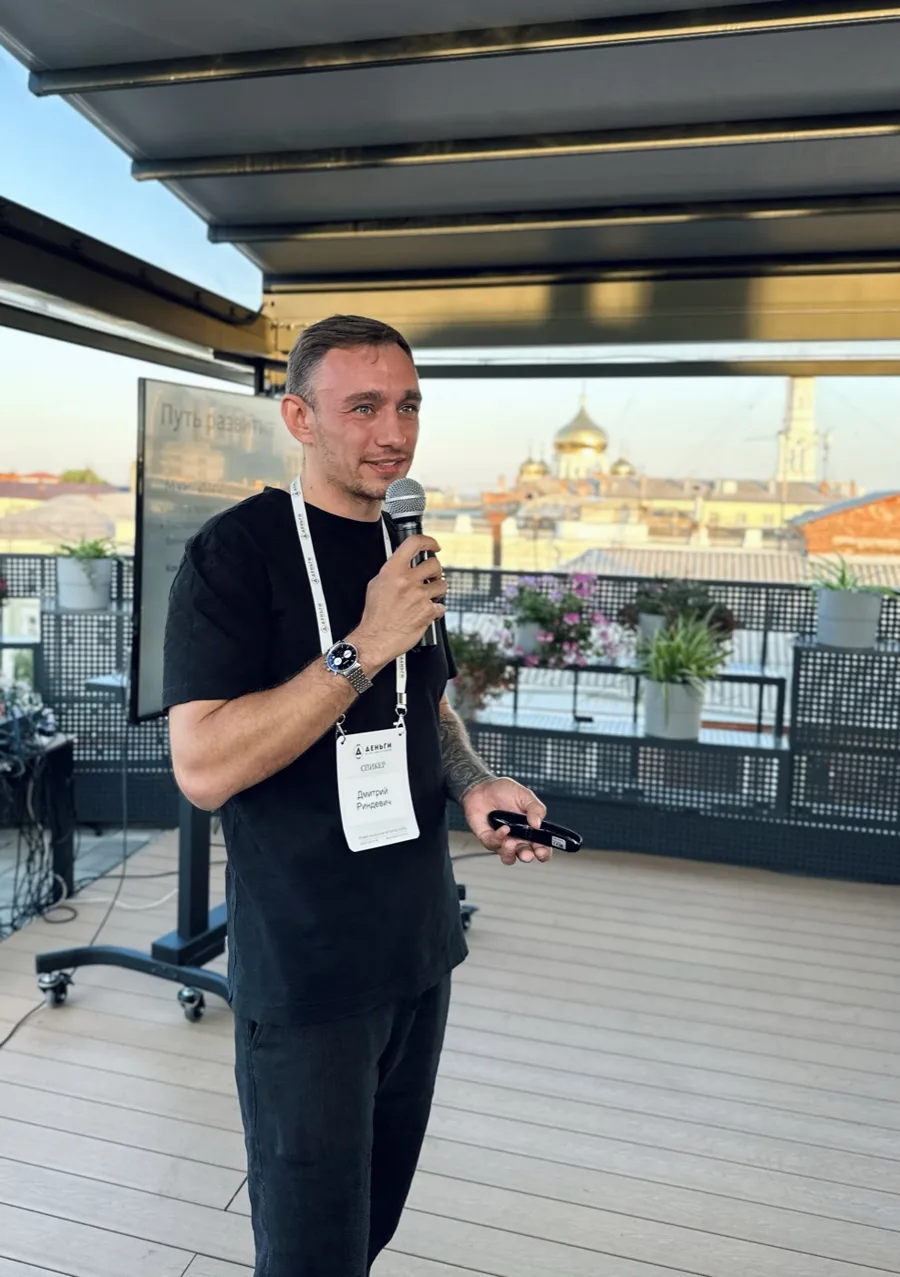 Dmitry Rindevich, founder of Tvoy Sklad, speaking with a microphone on a rooftop stage at a business event