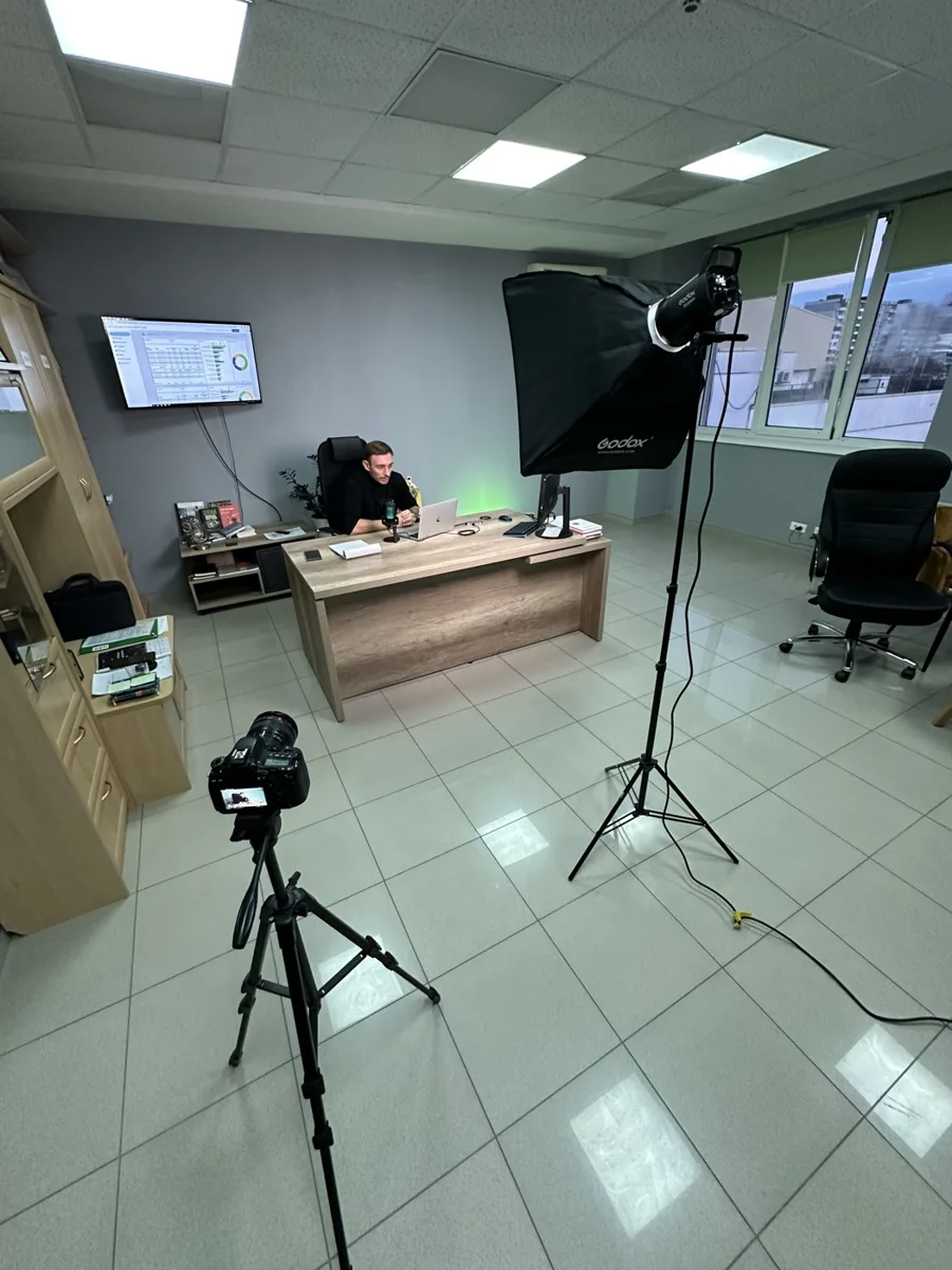 Filming a live stream in the Tvoy Sklad office: the founder at his desk, a camera on a tripod and a softbox light in front, the financial model on a TV screen behind him